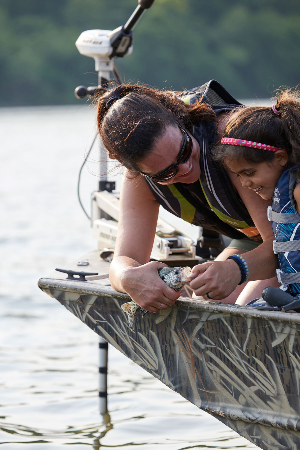 mother and daughter leaning off the side of a boat. The mother is showing the daughter a fish she caught.